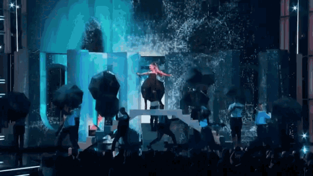 a group of people are dancing on a stage with umbrellas in the rain