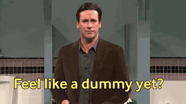 a man in a suit stands in a public restroom with the words feel like a dummy yet