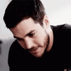 a close up of a man 's face with a beard wearing a black shirt and smiling .
