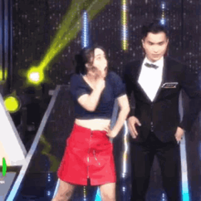 a man and a woman are dancing on a stage . the woman is wearing a red skirt .