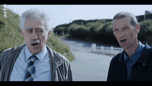 two men are standing next to each other on a road with a sign that says rtl