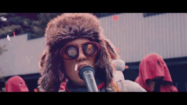 a person wearing a fur hat and sunglasses is holding a microphone
