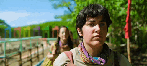 a young boy wearing a bandana and a backpack is standing in front of a girl .
