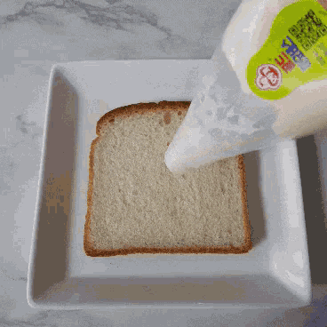 a bottle of mayonnaise is being poured onto a piece of bread on a white plate