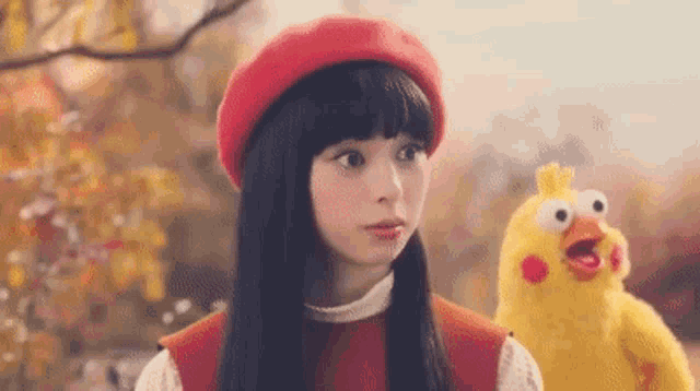 a woman in a red beret is standing next to a yellow stuffed chicken .