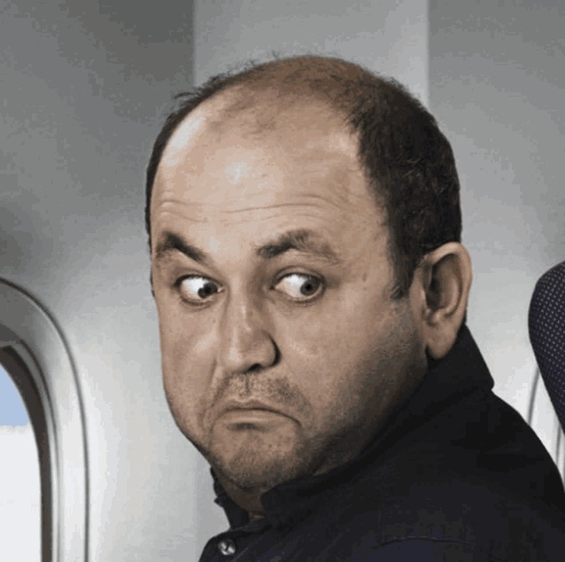 a bald man sitting on an airplane making a face