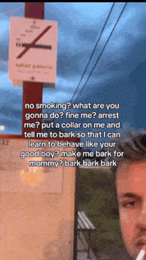 a man is smoking a cigarette in front of a sign that says no smoking