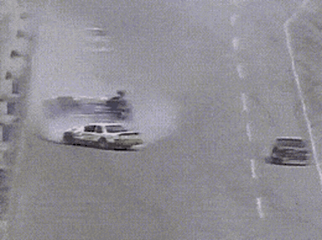 a white car is driving down a highway with a black car on the ground