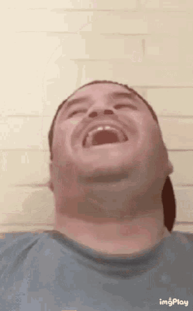 a man is laughing with his mouth open in front of a white brick wall ..