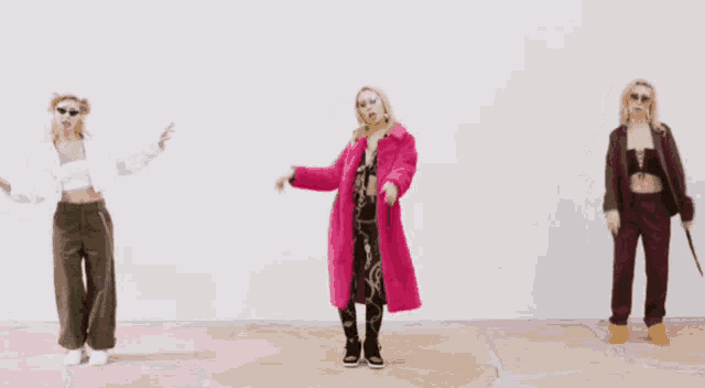 three women in different outfits are dancing in front of a wall