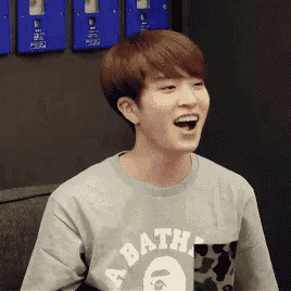 a young man wearing a bathing ape t-shirt is laughing with his mouth open .