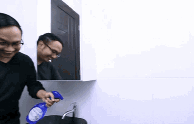a man is holding a spray bottle in front of a bathroom sink .