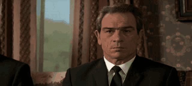 a man in a suit and tie is sitting in front of a window