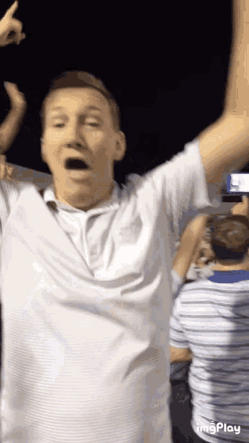 a man in a white shirt holds his arms in the air
