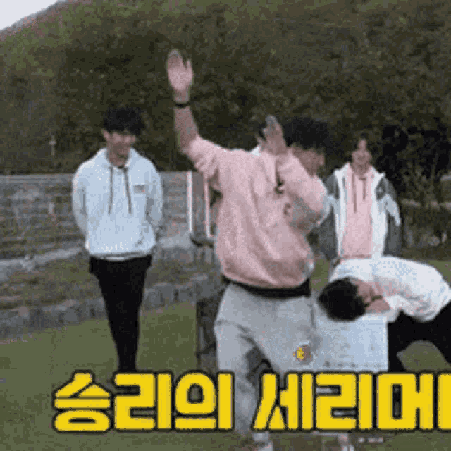 a group of people are standing in a field with a man in a pink sweatshirt dancing .