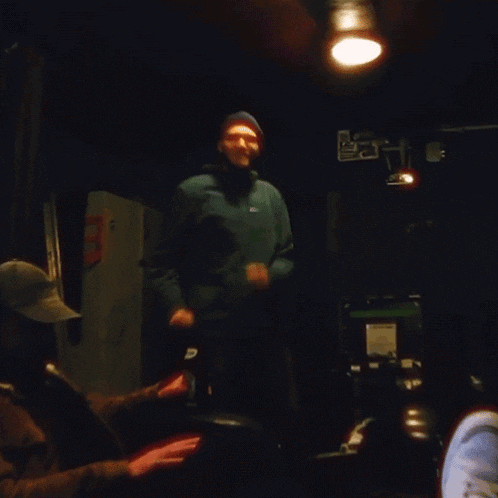 a man in a blue jacket is standing in a dark room with a sign that says ' a & a ' on it