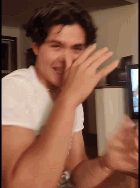 a man in a white shirt is covering his face with his hands