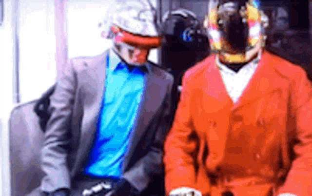 a man in a suit and a man in a red jacket are sitting next to each other on a train .