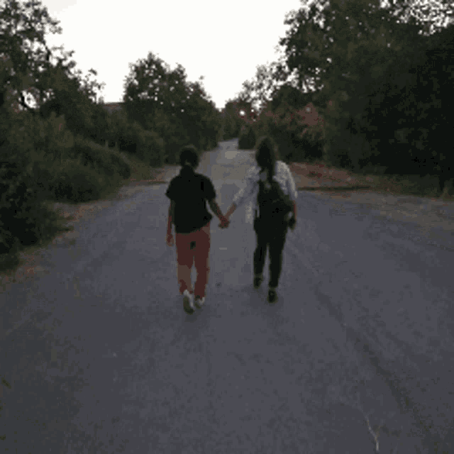 two people walking down a road holding hands with trees in the background