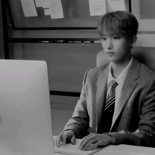 a man in a suit sits at a desk typing on a keyboard