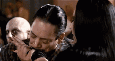 a man is kissing a woman 's hand while holding a knife in his mouth .