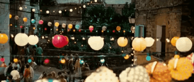 a crowd of people are walking down a street with lanterns hanging from a string