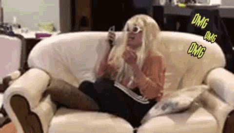a woman in a blonde wig is sitting on a white couch talking on a cell phone .