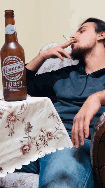 a man is smoking a cigarette next to a bottle of bomonti filtresiz