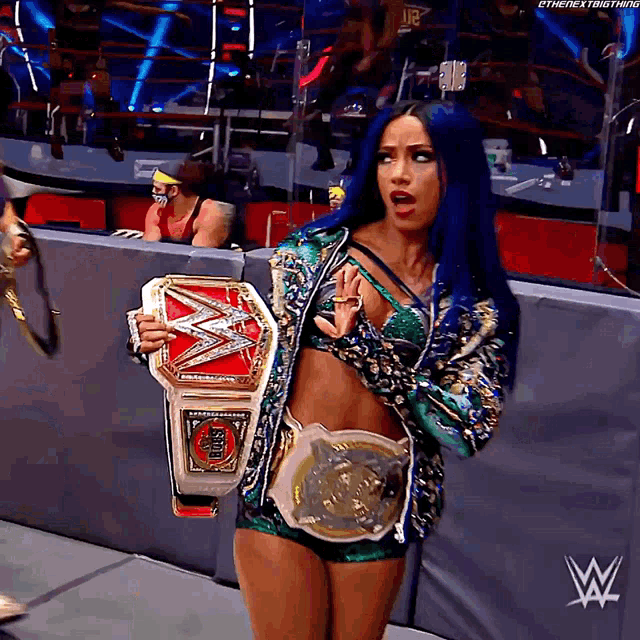 a female wrestler with blue hair is holding a wrestling championship belt