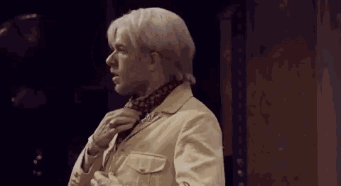 a man with white hair and a scarf around his neck is standing in a room .