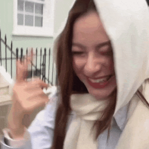 a woman wearing a scarf and a hood is smiling and waving .