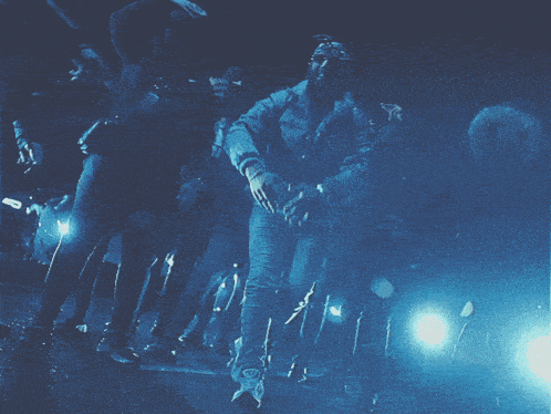 a group of people are dancing in a dark room with a blue light behind them