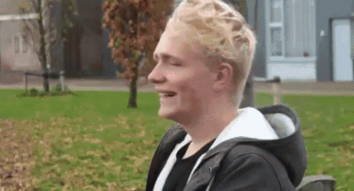 a young man is laughing in a park with a backpack .