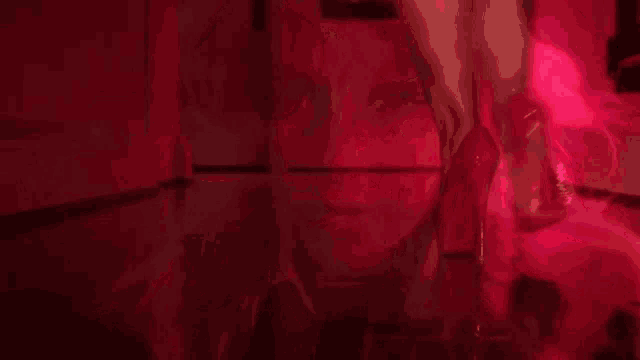 a woman with long blonde hair is standing in a dark room with red lights behind her .