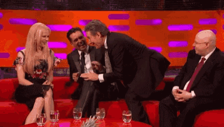 a group of people are sitting on a red couch talking to each other and laughing .