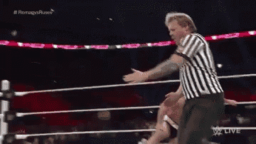 a referee in a striped shirt is standing in a wrestling ring with two wrestlers