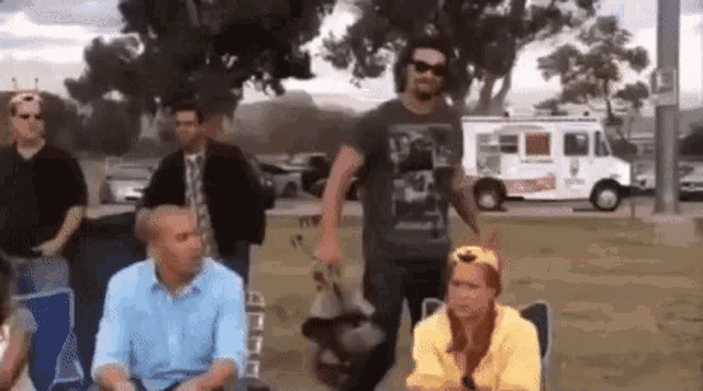 a group of people are sitting in chairs in a park while a man holds a dog in his arms .