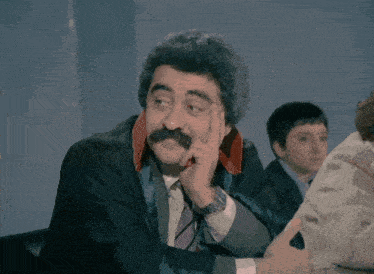 a man with a mustache is wearing a black suit and tie