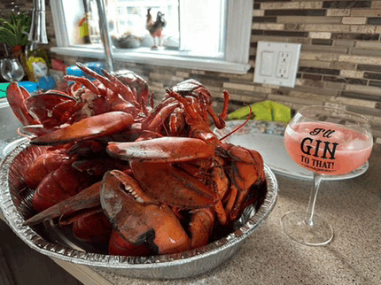 a bowl of lobsters sits on a counter next to a glass that says " i 'll gin to that "