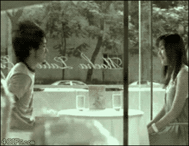 a man and a woman are looking at each other in front of a window that has the word love written in it