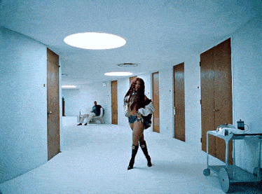 a woman is standing in a hallway with a man sitting in a chair behind her
