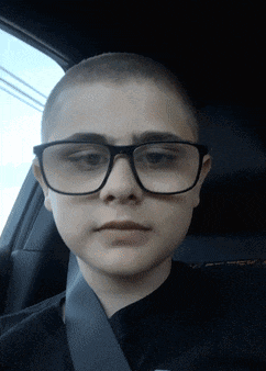 a boy with glasses and a shaved head is sitting in a car