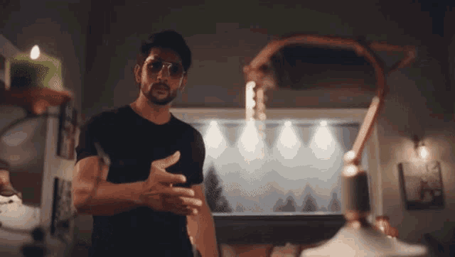 a man wearing sunglasses and a black shirt is standing in a room with a candle on a shelf .