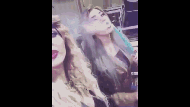 a woman with blue hair is smoking a hookah next to a woman with blonde hair .
