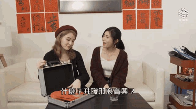 two women are sitting on a couch and one is holding a briefcase