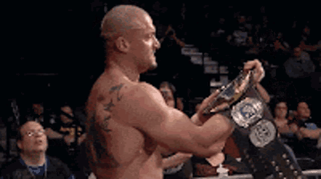 a shirtless wrestler is holding a wrestling belt in his hands