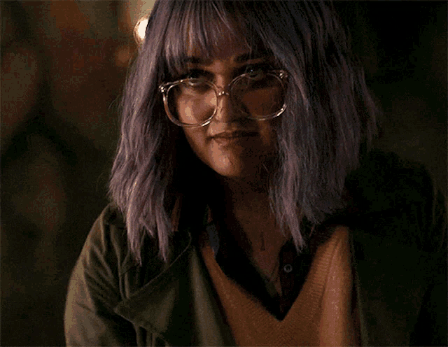 a woman with purple hair is wearing glasses and a green jacket .