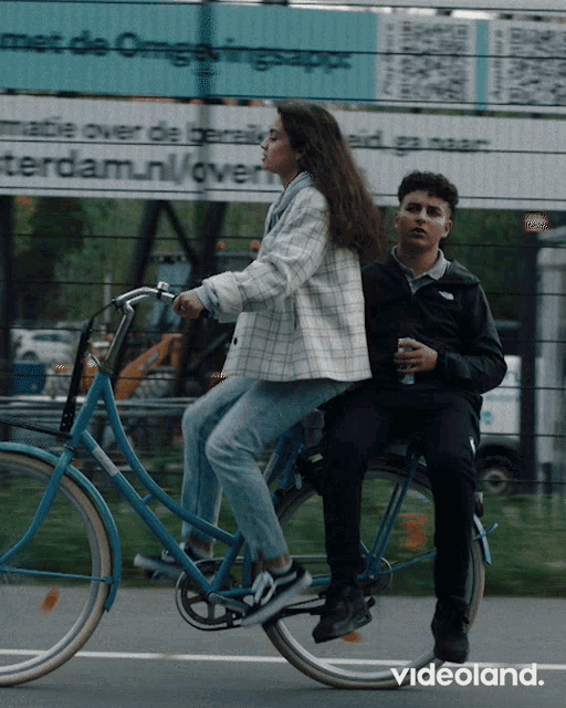 a man and a woman are riding a bike in front of a sign that says " met de omgevingsapp "
