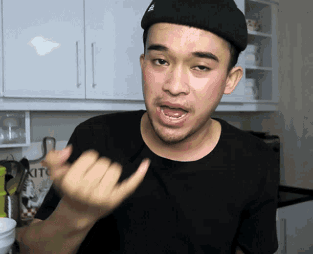 a man in a kitchen wearing a black shirt and a black hat with the word kitc on the front