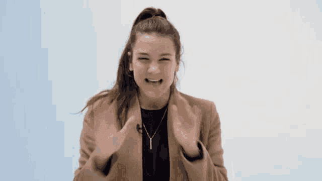 a woman in a brown jacket is making a funny face with her hands in the air